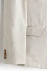 Blazer de lino slim fit color beige, con solapas de muesca, cierre de un botón central, bolsillos con solapa en el frente y bolsillo ojal en el pecho.
