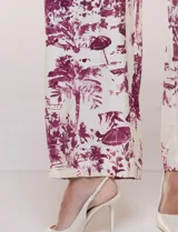 Enterito largo de calce fluido con escote en V cruzado, mangas 3/4 anchas, cintura elastizada con lazo ajustable y pantalón wide leg con bolsillos laterales. Estampado tipo toile de Jouy en tonos violeta sobre fondo blanco.