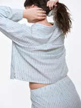 Camisa de dormir de popelina de algodón, con estampado de rayas verticales y pequeños motivos geométricos. Presenta cuello camisero, mangas largas y cierre frontal mediante lazos ajustables.