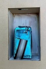 Billetera porta celular de cuero celeste con correa de tela a rayas negras y grises.