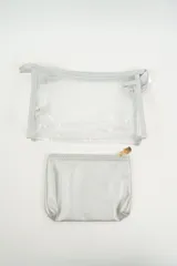 Neceser transparente con bordes y cierre en color beige claro, que incluye un neceser interior más pequeño de color plateado brillante.