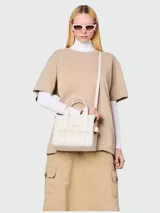 Bolso tote bag Marc Jacobs modelo The Leather Small Tote Bag, color blanco off-white, confeccionado en cuero. Cuenta con doble asa de mano, correa ajustable y desmontable para el hombro, y el texto "THE TOTE BAG" grabado en relieve en la parte frontal.