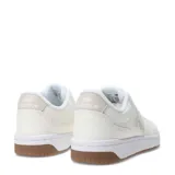 Championes urbanos New Balance de diseño minimalista, color blanco con detalles en tono crema. Presentan el logo N característico en el lateral, suela blanca con base de goma color caramelo y cierre mediante cordones.