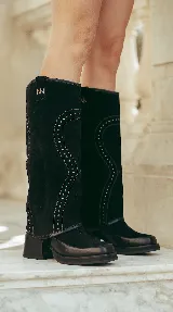 Bota alta de gamuza negra con diseño western, caña desmontable, taco ancho y detalles de tachas aplicadas.