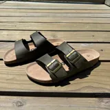 Sandalias de cuero sintético color verde militar, con plantilla marrón y hebillas metálicas doradas.