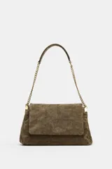 Bolso de hombro confeccionado en piel gamuzada marrón, con solapa frontal y cierre imantado. Cuenta con una correa combinada de cadena metálica dorada y tira de cuero, además de detalles de pespuntes.