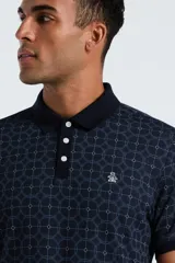 Polo de manga corta con cuello clásico y cierre frontal de dos botones. Presenta un estampado geométrico de círculos entrelazados en tonos azul marino y gris, con el logo de la marca bordado en el pecho.