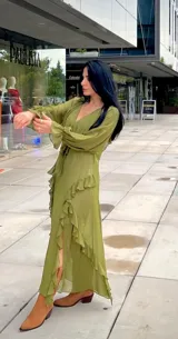 Vestido midi de gasa color verde oliva, con escote en V, mangas largas con puños elásticos y detalle de volados en la falda con abertura lateral.