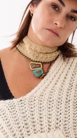 Choker tejido a mano en crochet color beige, con cadena metálica dorada y dijes colgantes con incrustaciones de piedras en tonos turquesa y detalles ornamentales.