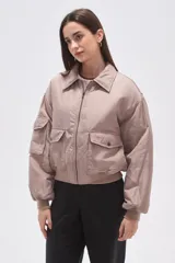 Campera tipo bomber color beige, confeccionada en poliéster, con cierre frontal, cuello camisero, bolsillos frontales con solapa y bolsillo adicional en la manga.