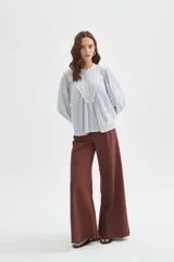 Blusa de algodón color beige, con cuello redondo y cierre frontal con botones. Presenta delicados bordados decorativos en tono tostado sobre el pecho y los hombros, mangas largas abullonadas con puños ajustados y diseño holgado.
