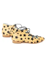 Semibotín de piel de pony con estampado de estrellas negras sobre fondo ocre. Presenta un diseño con abertura escotada, cierre de cordones negros a contraste y punta afilada. Incluye cuña interna y suela de cuero.