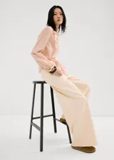 Blusa de seda color rosa pálido con volados frontales, cuello redondo y mangas largas con puños elásticos.
