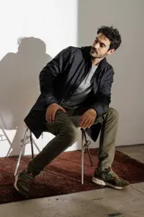 Campera impermeable verde con capucha, cierre frontal con botones a presión y bolsillos laterales con solapa.