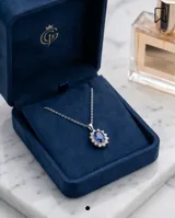 Collar de cadena fina de plata 925 con dije colgante en forma ovalada, compuesto por una piedra central de zafiro rodeada por pequeñas circonias brillantes.