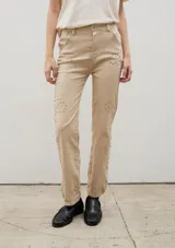 Pantalón de denim negro con diseño de tachas metálicas distribuidas en patrones curvos. Presenta un corte recto y tiro medio.