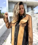 Sobre camisa de gamuza con diseño de paneles verticales en colores marrón, tostado y negro. Presenta cuello clásico, cierre frontal con botones metálicos y un bolsillo en el pecho con solapa.