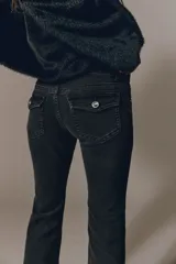 Jean de denim negro elástico, de tiro bajo y corte acampanado desde la rodilla. Cuenta con bolsillos delanteros y bolsillos traseros con solapa y botón.