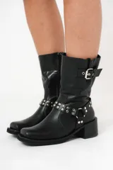 Bota biker de caña media color negro, con hebilla en la parte superior y detalle de aro y tachas en la parte inferior.