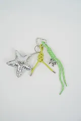 Llavero de diseño multicolor con mosquetón en forma de corazón, dije de estrella plateada acolchada, tira de cuero sintético verde lima con nudo y cordón verde estampado con dije de lazo plateado.