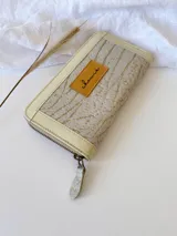 Billetera grande de cuero con diseño bicolor en tonos beige y crema, con textura grabada en el cuerpo principal y detalles en cuero liso. Cuenta con cierre perimetral metálico y tirador de cuero.