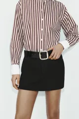 Falda pantalón de tiro medio color negro, con bolsillos delanteros y detalle de cinturón integrado con hebilla metálica dorada. Cierre frontal con cremallera y gancho.