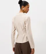 Camisa de manga larga confeccionada en satén color beige, con cuello clásico, cierre frontal de botones y pliegues decorativos en la cintura que realzan la silueta.