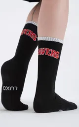 Medias 3/4 de algodón color negro, con el texto 'RAVERS' bordado en rojo en la parte superior y logo 'LUXO' en la planta del pie. Presentan un borde superior acanalado en color gris claro.