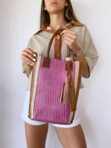 Bolso matero de cuero color fucsia y marrón con textura croco, doble asa de mano marrón y detalle de borlas de cuero marrón.