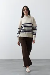 Polera de tejido de punto con diseño a rayas horizontales en color azul marino sobre base beige. Presenta cuello alto, mangas largas con puños acanalados y una silueta relajada.