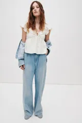 Blusa corta blanca en punto pointelle con textura, escote corazón, mangas cortas circulares, detalle cut-out con cordón de ajuste en el busto y diseño acampanado con costura fruncida.
