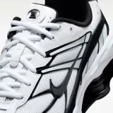 Zapatilla deportiva Nike Shox Ride 2, color blanco con detalles en negro y acentos celestes pálidos. Presenta una estructura de soporte en la parte superior y tecnología de amortiguación Nike Shox visible en el talón.