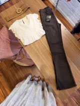 Jeans de corte flare color marrón oscuro, confeccionados en denim, con tiro medio, bolsillos clásicos y detalle de dobladillo deshilachado con pequeña abertura lateral en los tobillos.