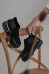 Botas tipo chelsea de caña baja, confeccionadas en una combinación de cuero gamuzado y cuero texturizado en tono marrón oscuro. Presentan una suela track de plataforma gruesa y elásticos laterales negros.