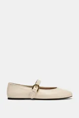 Zapato plano tipo bailarina confeccionado en piel de color crudo, con tira en el empeine y hebilla metálica dorada ajustable. Presenta puntera redonda y suela plana.