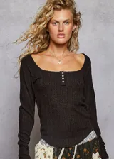 Blusa de manga larga en color negro, confeccionada en tejido de punto con textura acanalada. Presenta un escote cuadrado y una pequeña abertura frontal con cierre de botones.