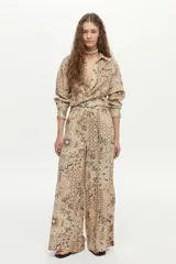 Pantalón de pierna ancha y tiro medio, confeccionado en mezcla de lino y viscosa, con cintura elástica y cordón ajustable. Presenta un estampado artesanal en tonos beige y marrón.