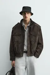 Cazadora de corte relajado confeccionada en piel con acabado de ante. Presenta cuello subido, cierre frontal de cremallera oculta por solapa con botones a presión, bolsillos de plastrón con solapa en el pecho y bolsillos de vivo en la cadera. Incluye trabillas en los hombros, mangas largas con puños abotonados y bajo con elástico.