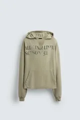Sudadera de corte relajado color verde oliva con efecto lavado. Presenta capucha con abertura frontal, bolsillo tipo canguro, mangas largas con puños de rib y bajo con acabado irregular. Incluye estampado frontal con texto.