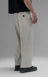 Pantalón de corte oversize confeccionado en microfibra técnica con sutil elasticidad. Presenta cintura elástica, bolsillos laterales y un bolsillo cargo con cierre de broche snap. Incluye un sistema de elásticos con tancas en los tobillos para regular la apertura y modificar la silueta.