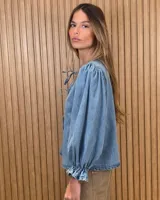 Camisa color beige de lino con mangas abullonadas tres cuartos y cierre frontal mediante múltiples lazos para atar.