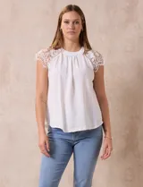 Blusa blanca de crepe, con cuello redondo y mangas cortas con apliques de crochet. La espalda presenta una abertura con ojal y botón.
