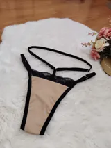 Tanga de diseño moderno confeccionada en lycra color beige con detalles de encaje negro en la parte superior. Presenta tiras elásticas ajustables en la cintura y bordes reforzados en color negro.