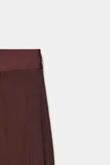 Pantalón de tiro medio con diseño tipo pareo, confeccionado en tejido satinado con acabado arrugado. Presenta pernera recta, cierre frontal con botón a presión y cremallera lateral oculta.