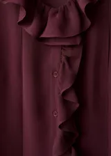 Blusa de viscosa color bordó, con diseño de volantes frontales, cuello redondo con detalle de fular y mangas largas con puños abotonados.