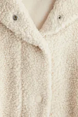 Campera de sherpa con cuello alto, hombros caídos, cierre frontal oculto con botones a presión y bolsillos laterales insertados. Diseño forrado con puños elásticos.