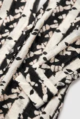 Blusa manga larga de corte recto con cuello camisero y escote en V profundo. Presenta un estampado vertical de rayas con motivos abstractos en tonos marrón oscuro sobre fondo beige.