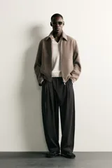 Pantalón de corte balloon fit en color gris oscuro, confeccionado en tejido con viscosa. Presenta pliegues frontales, cintura ajustable con cinturón integrado, bolsillos laterales y bolsillos traseros de doble vivo. Cierre frontal con cremallera y botón.