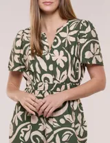 Enterito verde oscuro con estampado floral y abstracto en tono beige, de corte suelto y caída fluida. Presenta escote en V, mangas cortas, cintura elastizada con faja fruncida y pantalón crop de pierna ancha con bolsillos laterales.