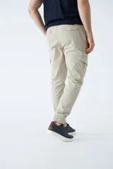 Pantalón cargo color verde oliva, de corte slim, con cintura elastizada y cordón ajustable. Presenta bolsillos laterales tipo cargo con botones y puños elásticos en los tobillos.